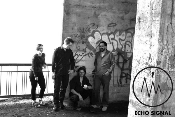 Black and white photograph of Rachel, Adam, Phaedrus, and Ben (Echo Signal in 2014) beside a graffitied bridge pillar.