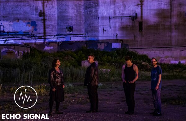 Phaedrus, John, Adam, and Charles (Echo Signal in 2016) standing apart in dry grass in front of a vast concrete grain silo at dusk, the whole scene cast in violet.